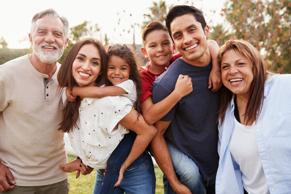 three-generation-hispanic-family-standing-in-the-park--smiling-to